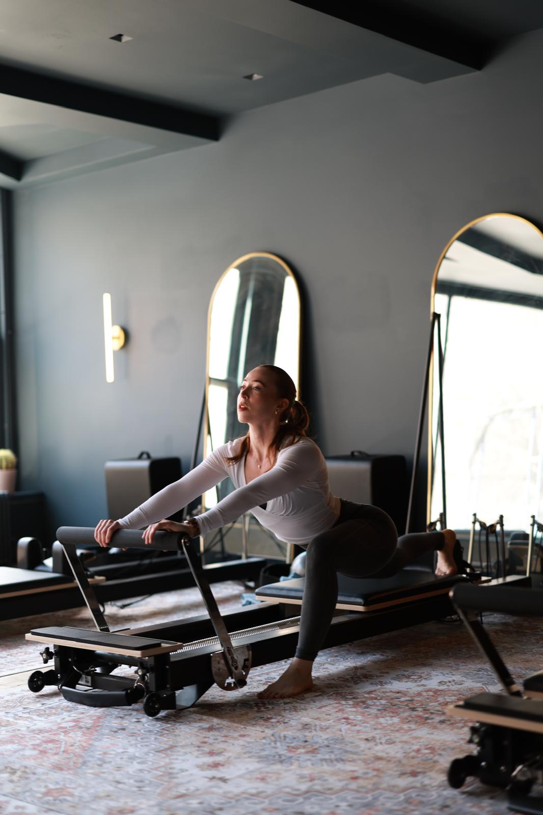 Erin stretching on a reformer in a sunlit pilates studio.