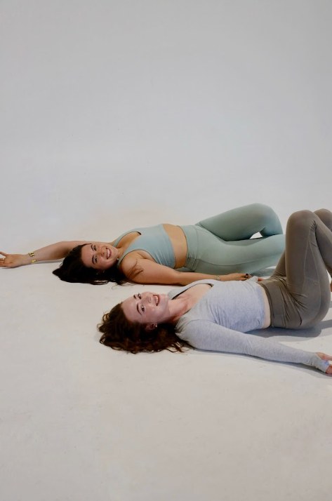 Two women lying back on the studio floor laughing after a workout.