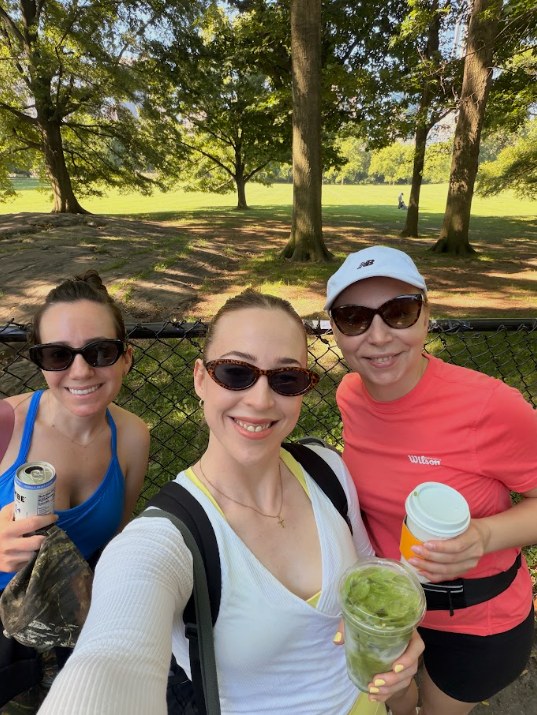 Erin and two friends in sunglasses smiling together in Central Park with matcha and coffee after a walk.